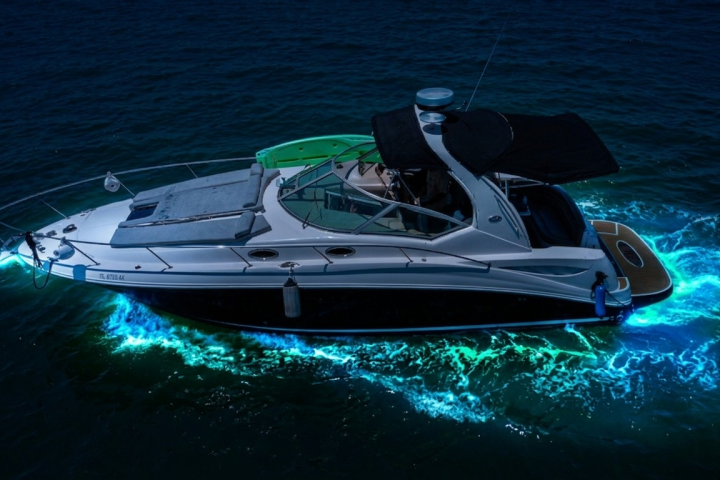 Boat with glowing blue underwater lights on dark water.