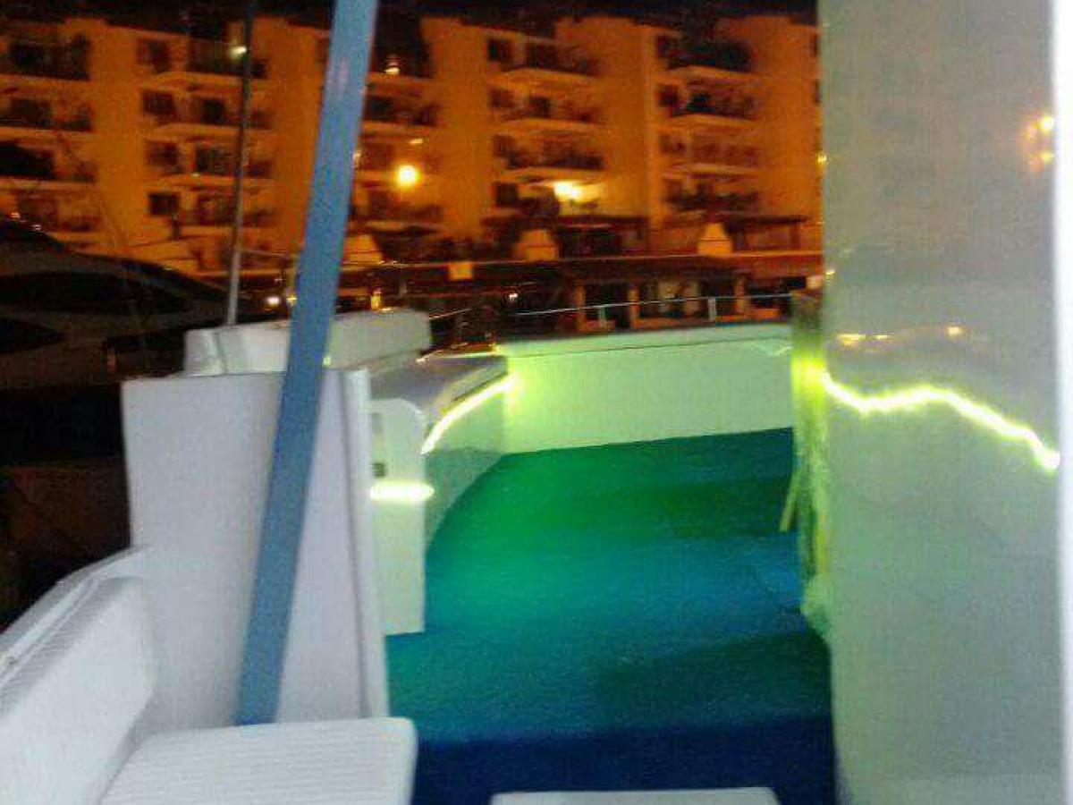 Boat deck at night with seating, illuminated buildings in background.