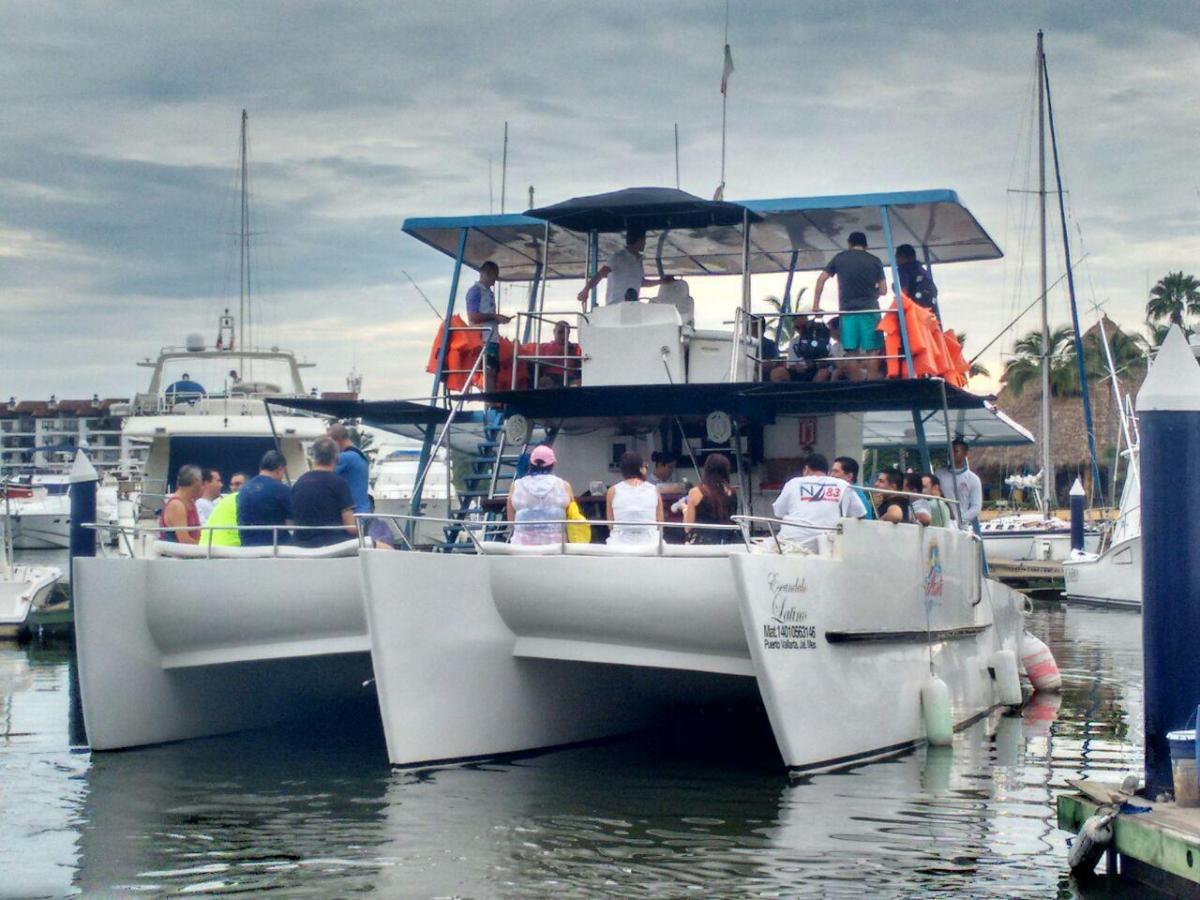 People on a docked multi-hull boat in a marina under a cloudy sky.
