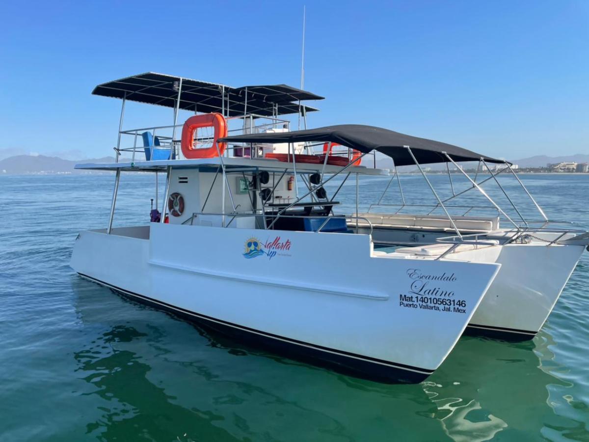 White passenger boat with canopies on calm water, mountains in the background.