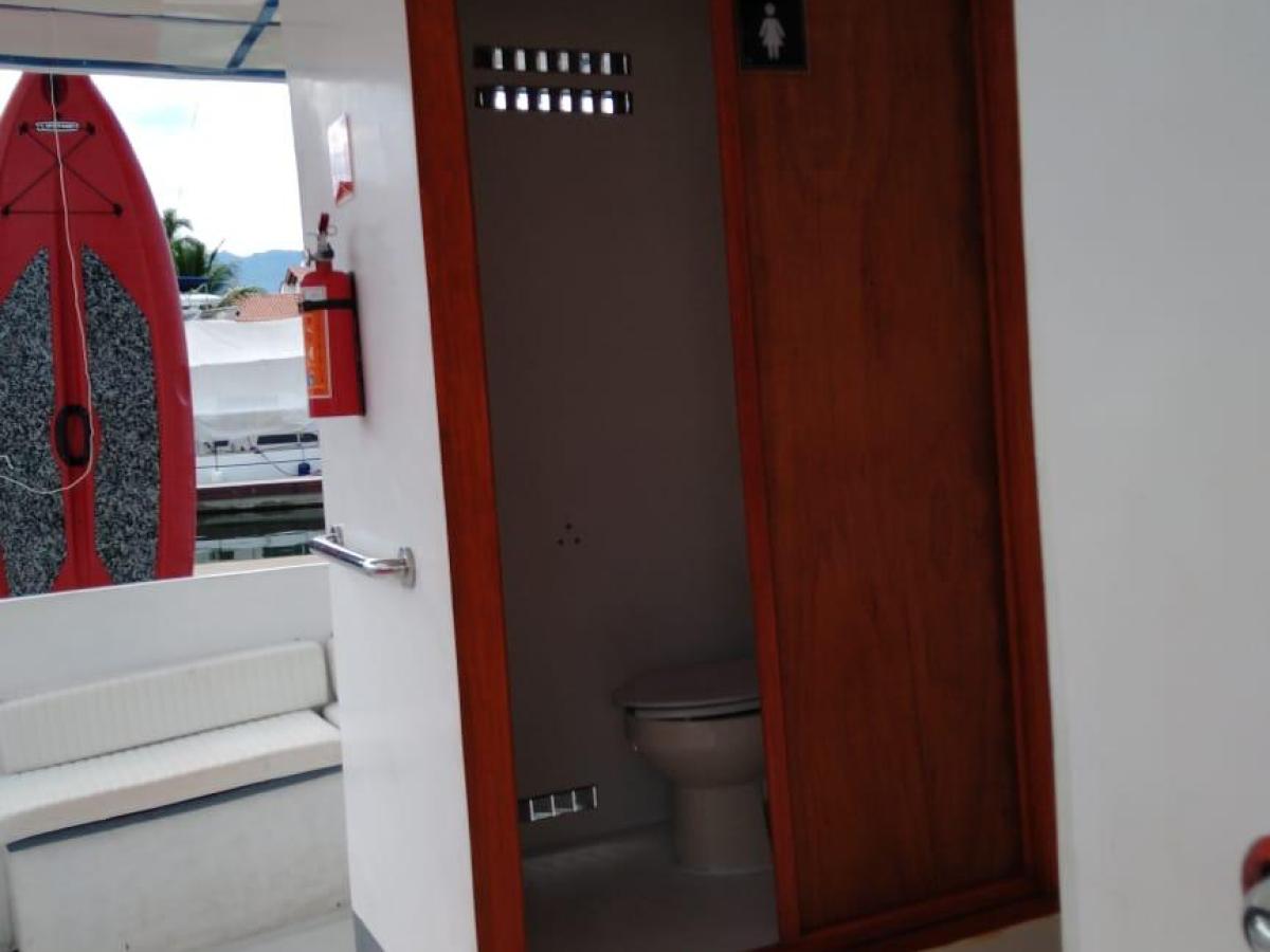 Boat restroom with wooden door, toilet visible; red surfboard in background.