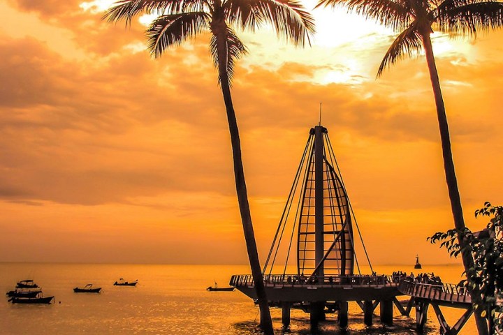 a sunset over a body of water next to a palm tree
