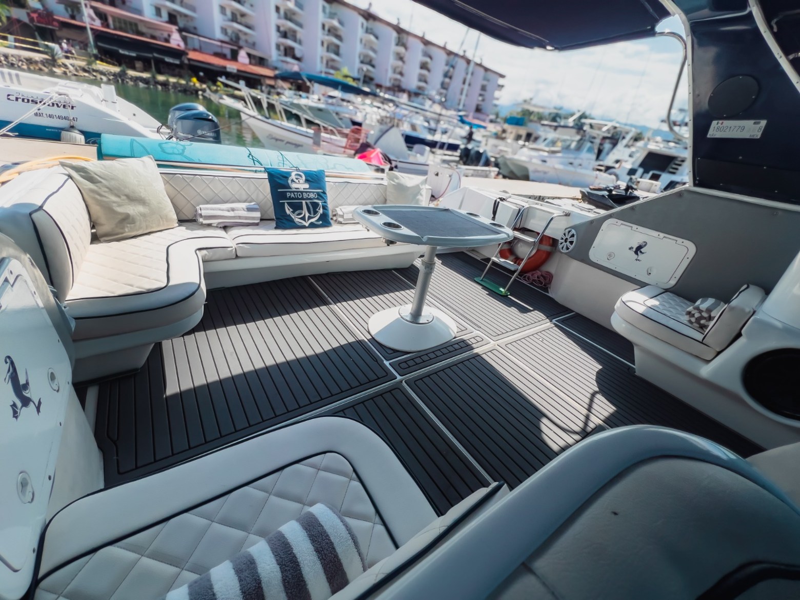 Yacht deck with cushioned seating, table, and marina view in background.