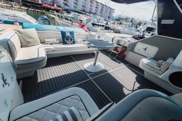 Yacht deck with cushioned seating, table, and marina view in background.