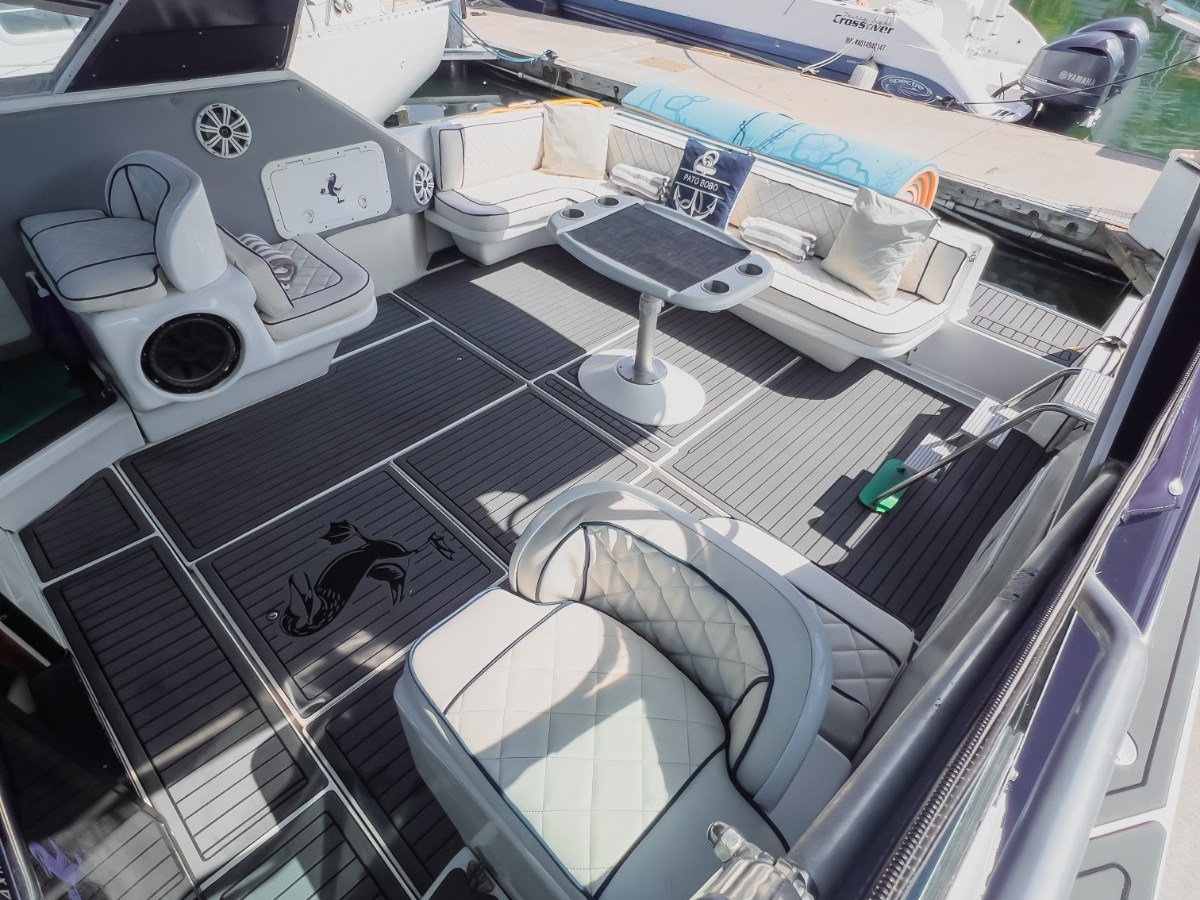 Luxury yacht deck with cushioned seating, table, and decorative floor, docked beside another boat.