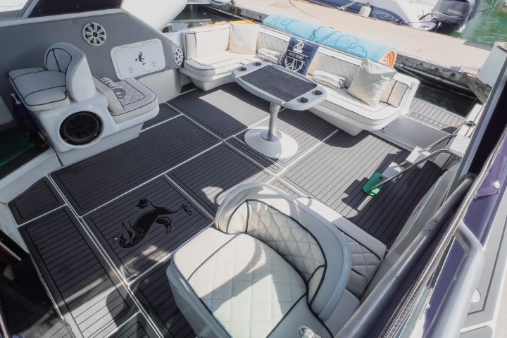 Luxury yacht deck with cushioned seating, table, and decorative floor, docked beside another boat.