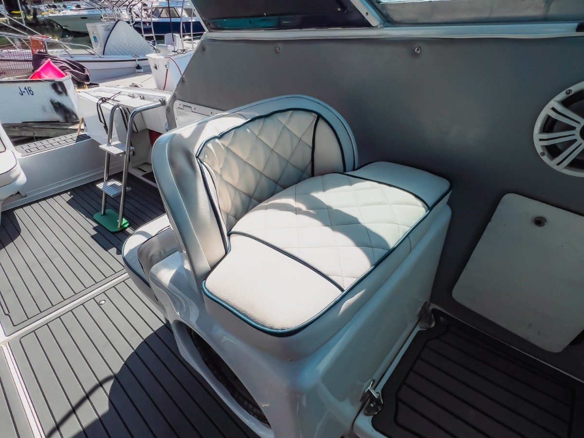 Boat interior with white cushioned seat and marina view in background.
