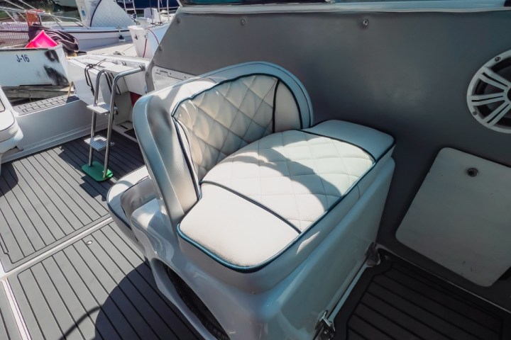 Boat interior with white cushioned seat and marina view in background.