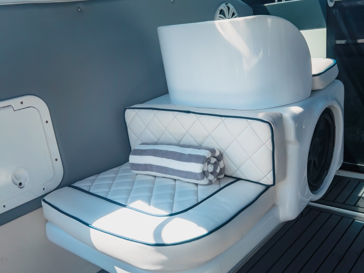 Luxury boat seat with white quilted cushion and striped towel, next to a window showing blue sky.