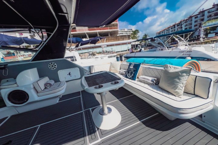 Luxurious yacht deck with cushioned seating, table, and marina view.