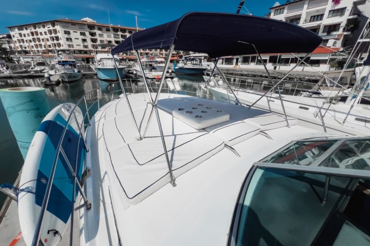 View of a yacht's deck with a blue canopy, docked in a marina with several boats and buildings in the background.