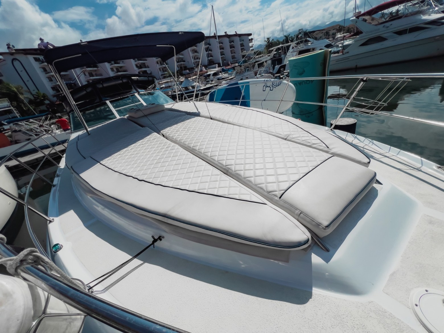 A boat with a cushioned deck area docked at a marina under a partly cloudy sky.