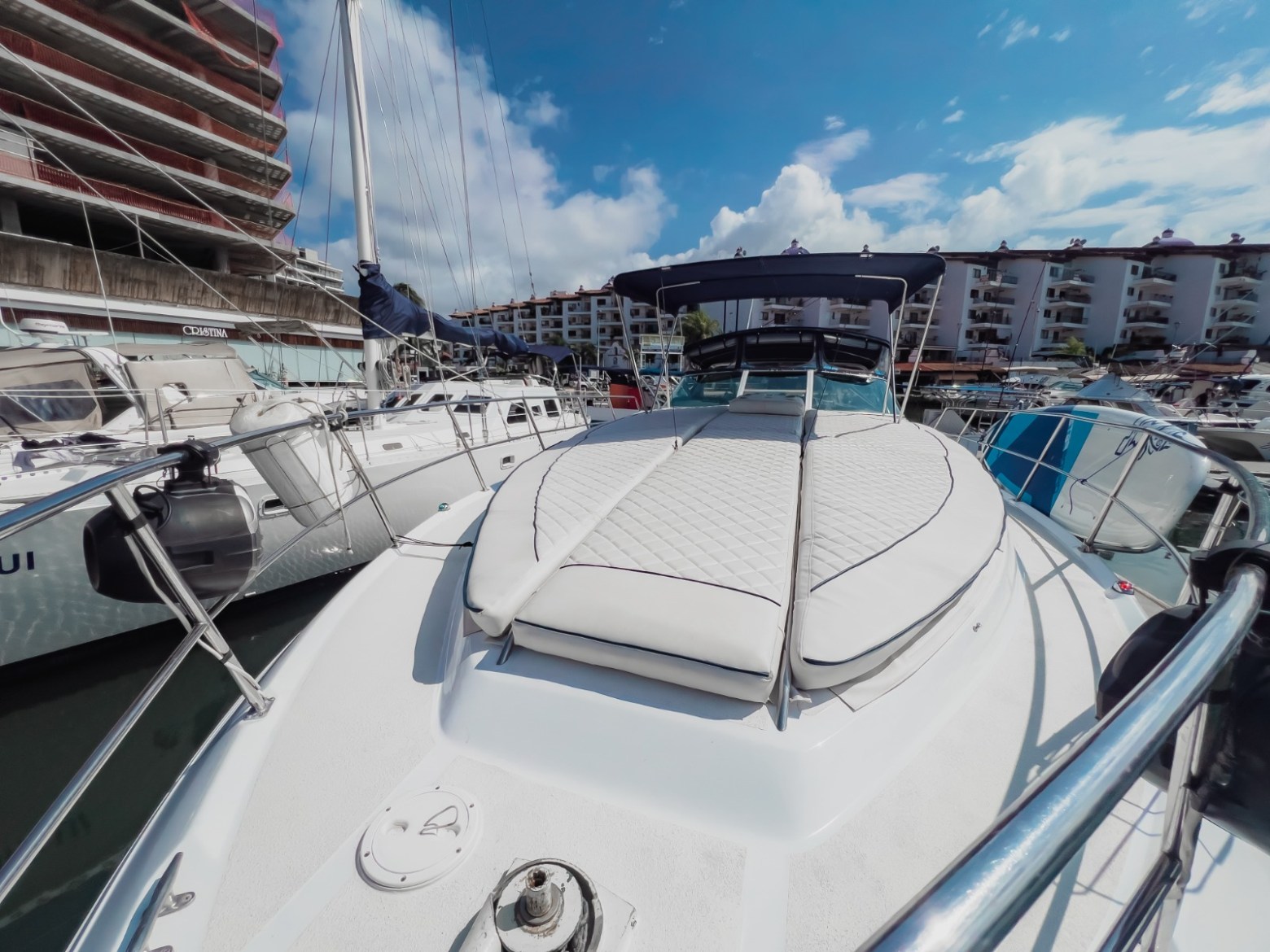 View of a luxury boat deck with padded seating docked in a marina under a blue sky.