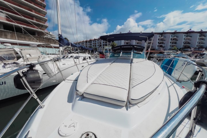 View of a luxury boat deck with padded seating docked in a marina under a blue sky.