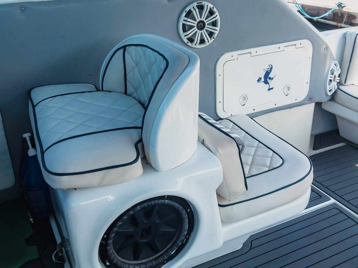 Boat interior with white cushioned seat, speaker, and storage panel.