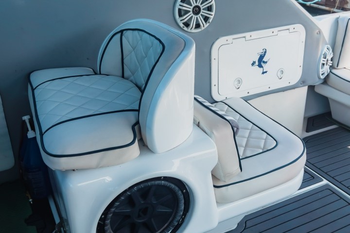 Boat interior with white cushioned seat, speaker, and storage panel.