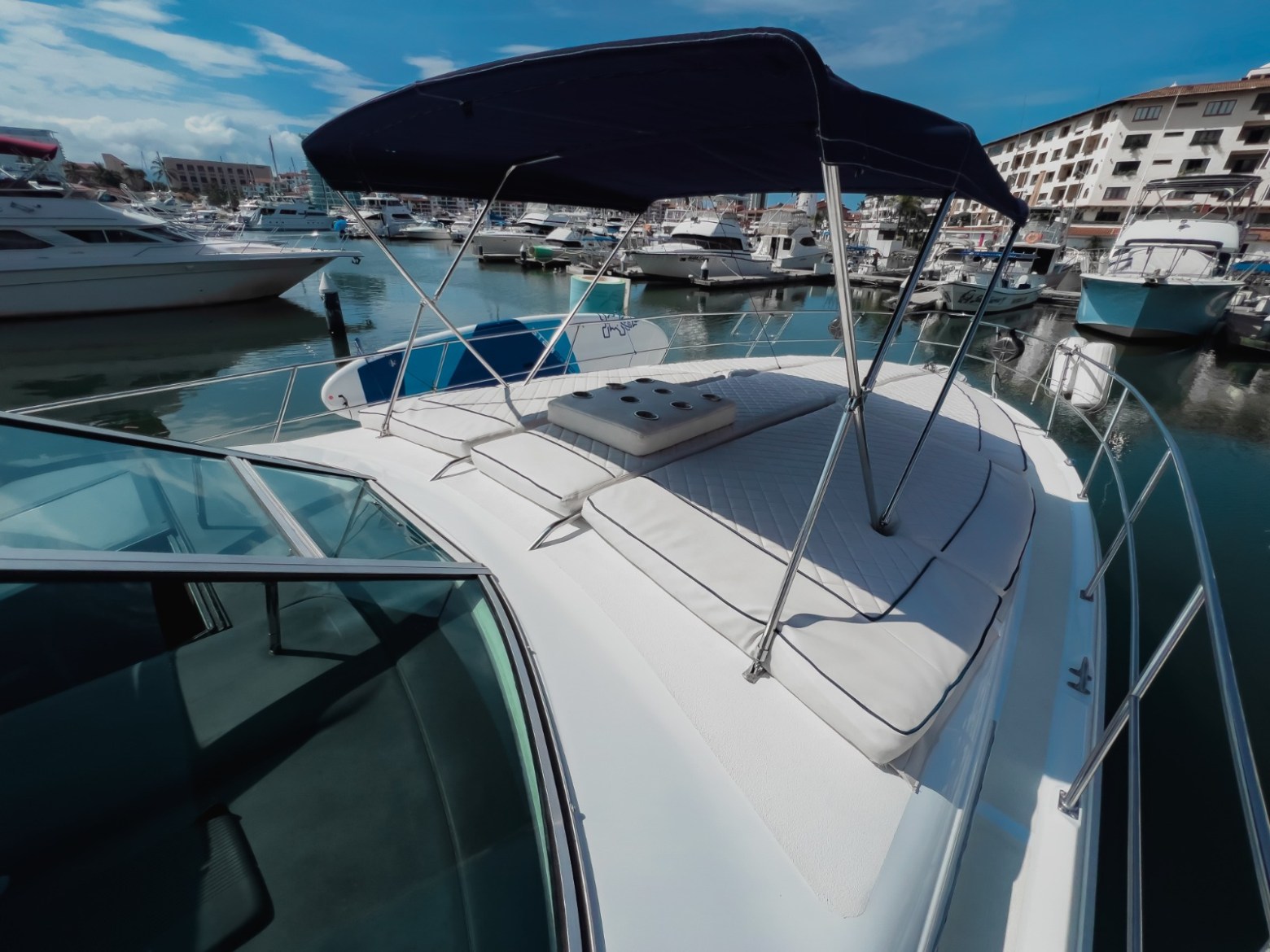 Boat with cushioned seating under canopy docked at marina with other boats.