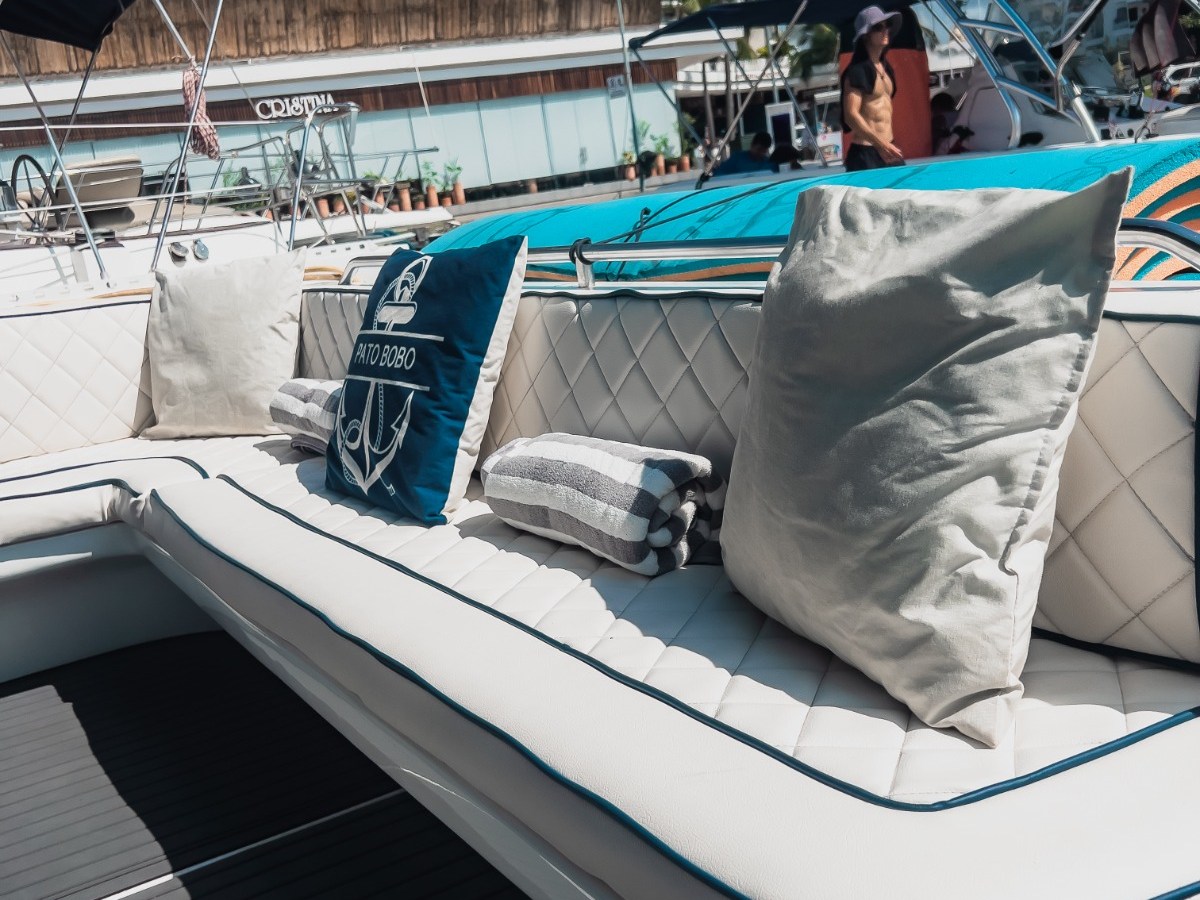 Boat interior with cushioned seating and pillows against a marina backdrop.