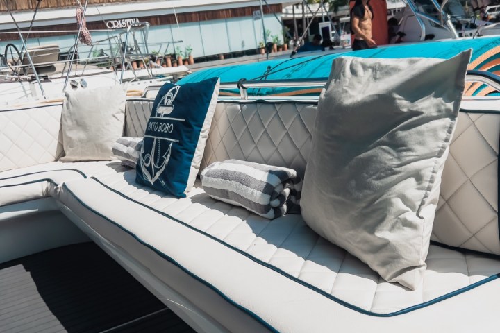 Boat interior with cushioned seating and pillows against a marina backdrop.
