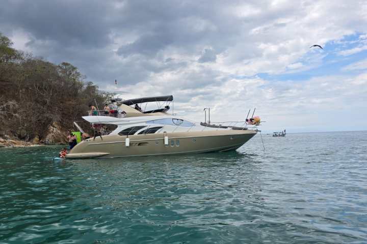 Luxury yacht on calm sea near rocky shoreline under cloudy sky.
