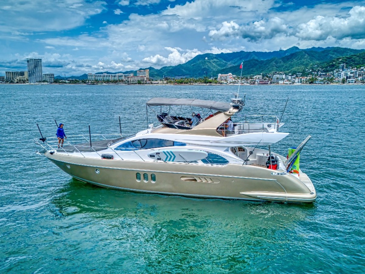Luxury yacht on calm water with city and mountains in the background.