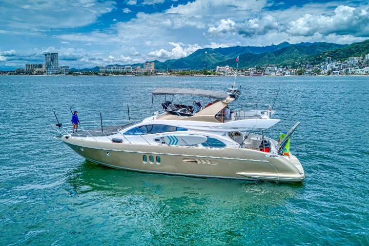 Luxury yacht on calm water with city and mountains in the background.