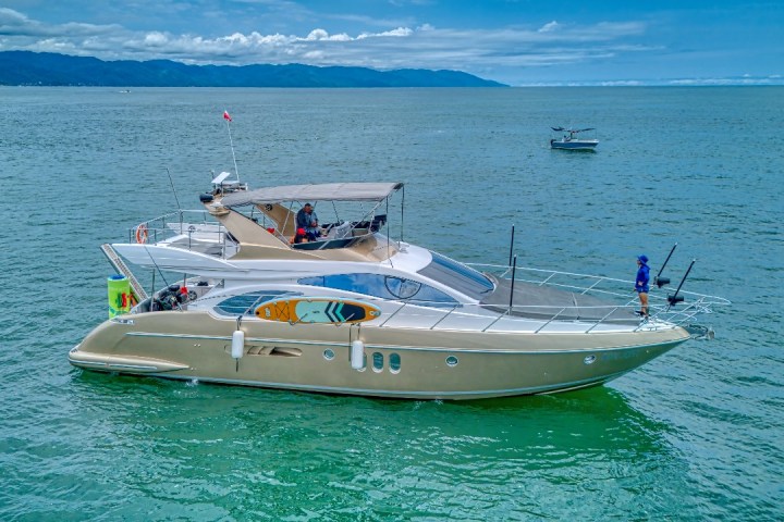 Luxury yacht on calm sea with hills in the background.
