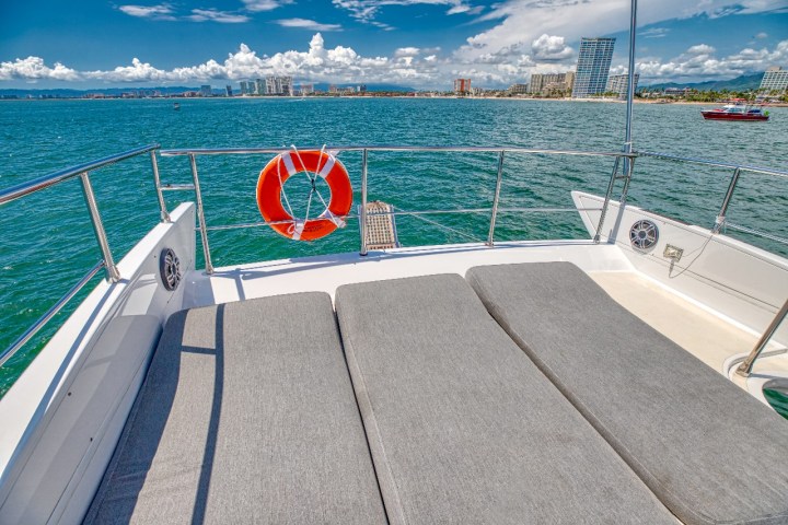 View from boat deck with cushions, facing ocean and city skyline.