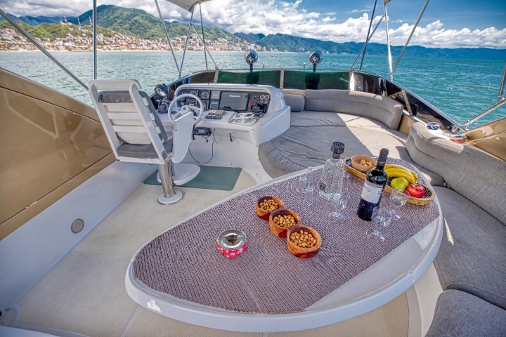 Luxury yacht deck with helm, snacks, wine, and sea view.