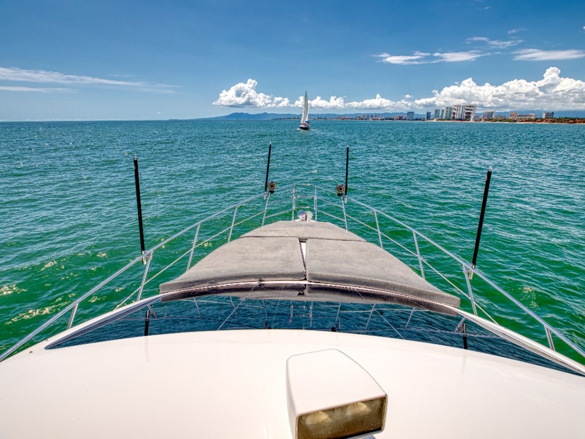 View from a boat's deck facing a sailboat in open sea under clear sky.
