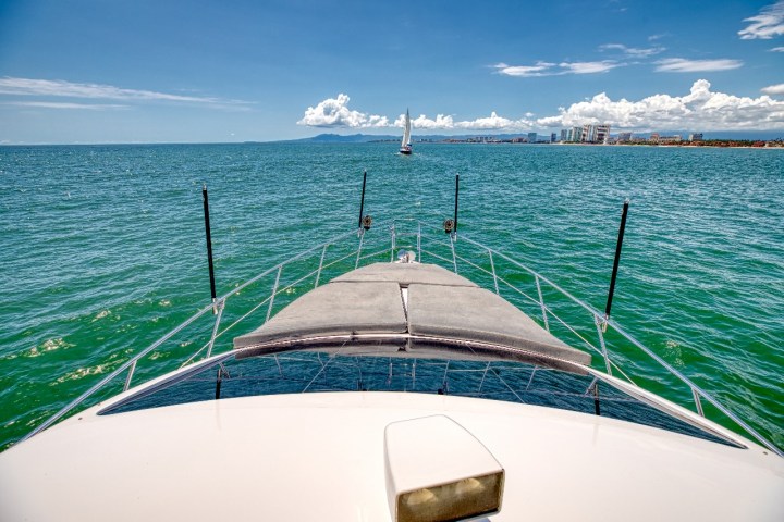 View from a boat's deck facing a sailboat in open sea under clear sky.