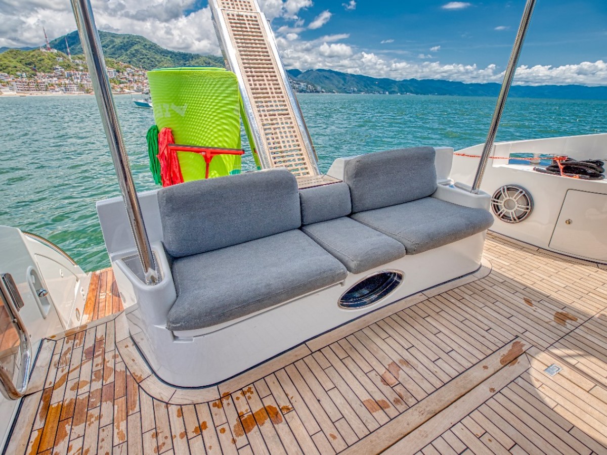 Boat deck with gray sofa, ocean view, and mountains in background.