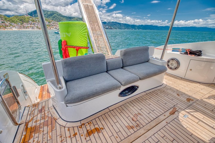 Boat deck with gray sofa, ocean view, and mountains in background.