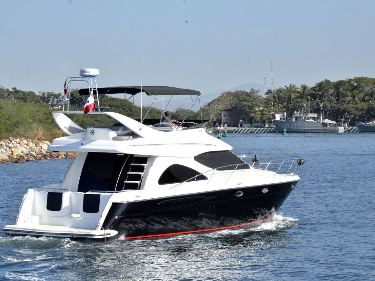 White motor yacht cruising on a calm waterway near a forested shore.