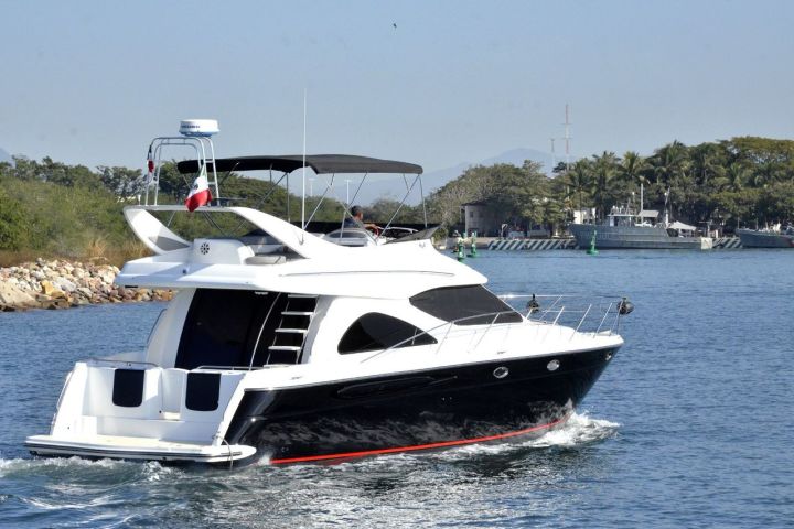 White motor yacht cruising on a calm waterway near a forested shore.