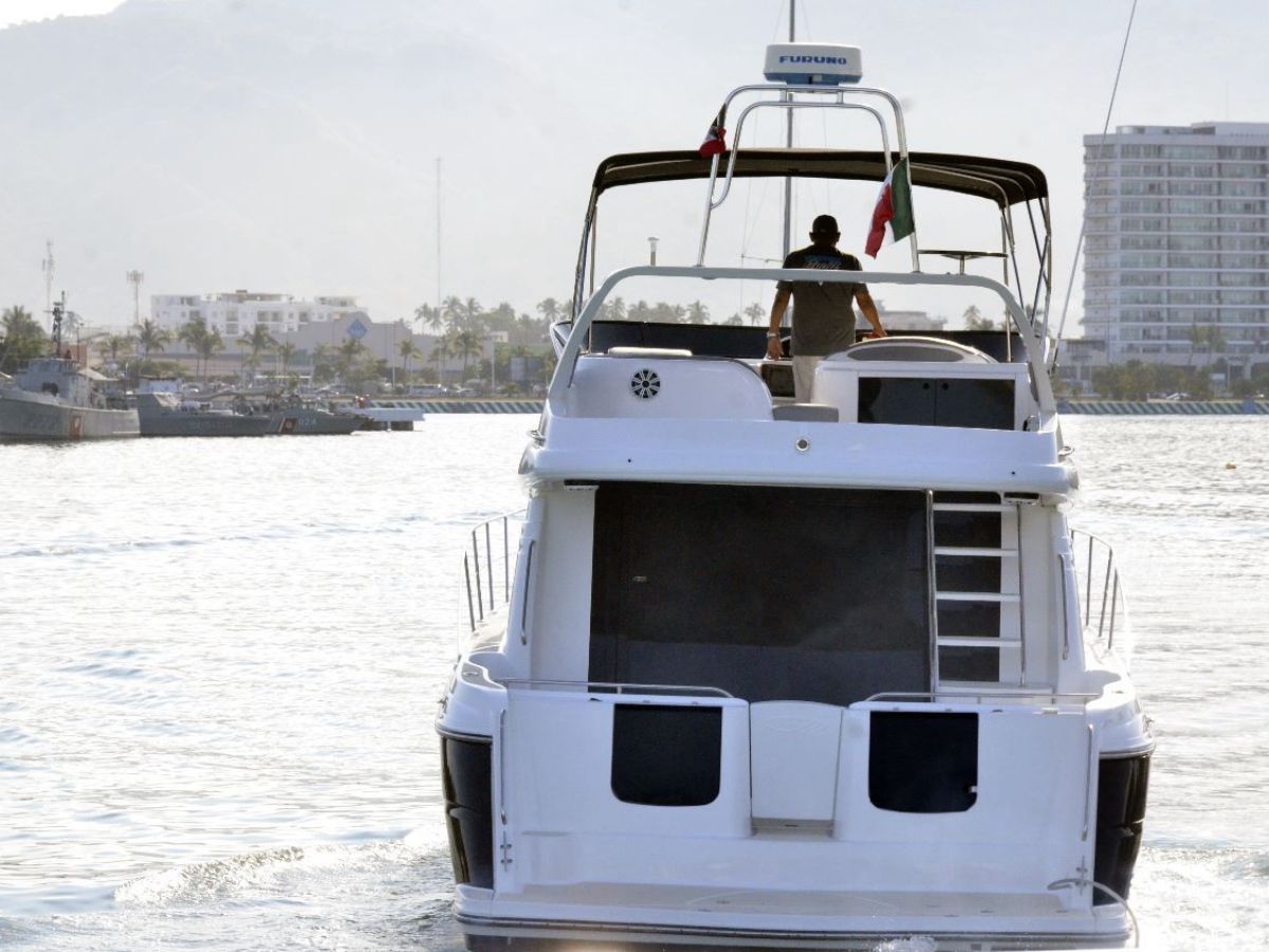 Person steering a yacht on a calm sea near a cityscape.