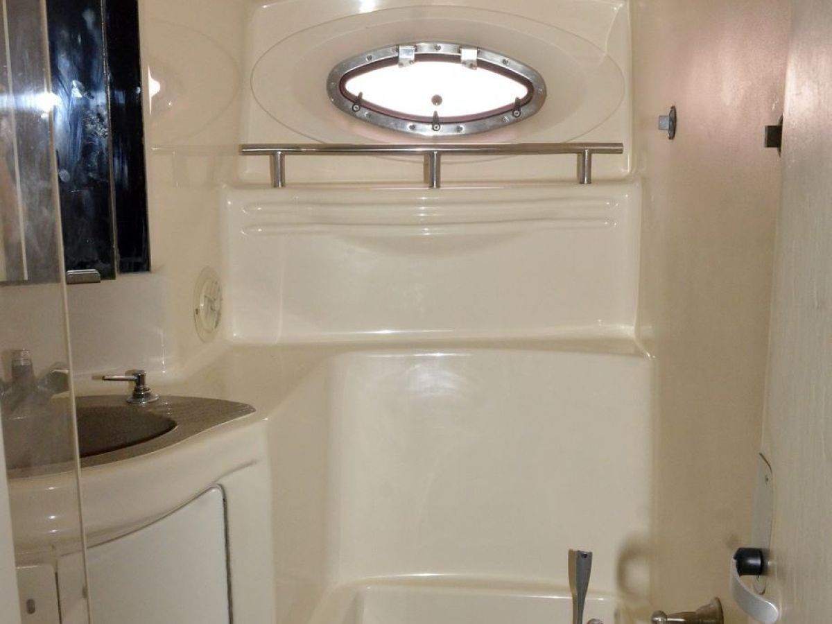 Compact boat bathroom with toilet, circular window, and small sink.