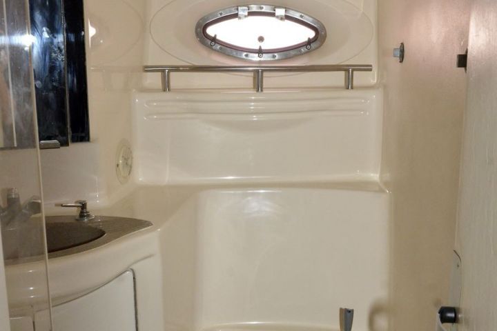 Compact boat bathroom with toilet, circular window, and small sink.