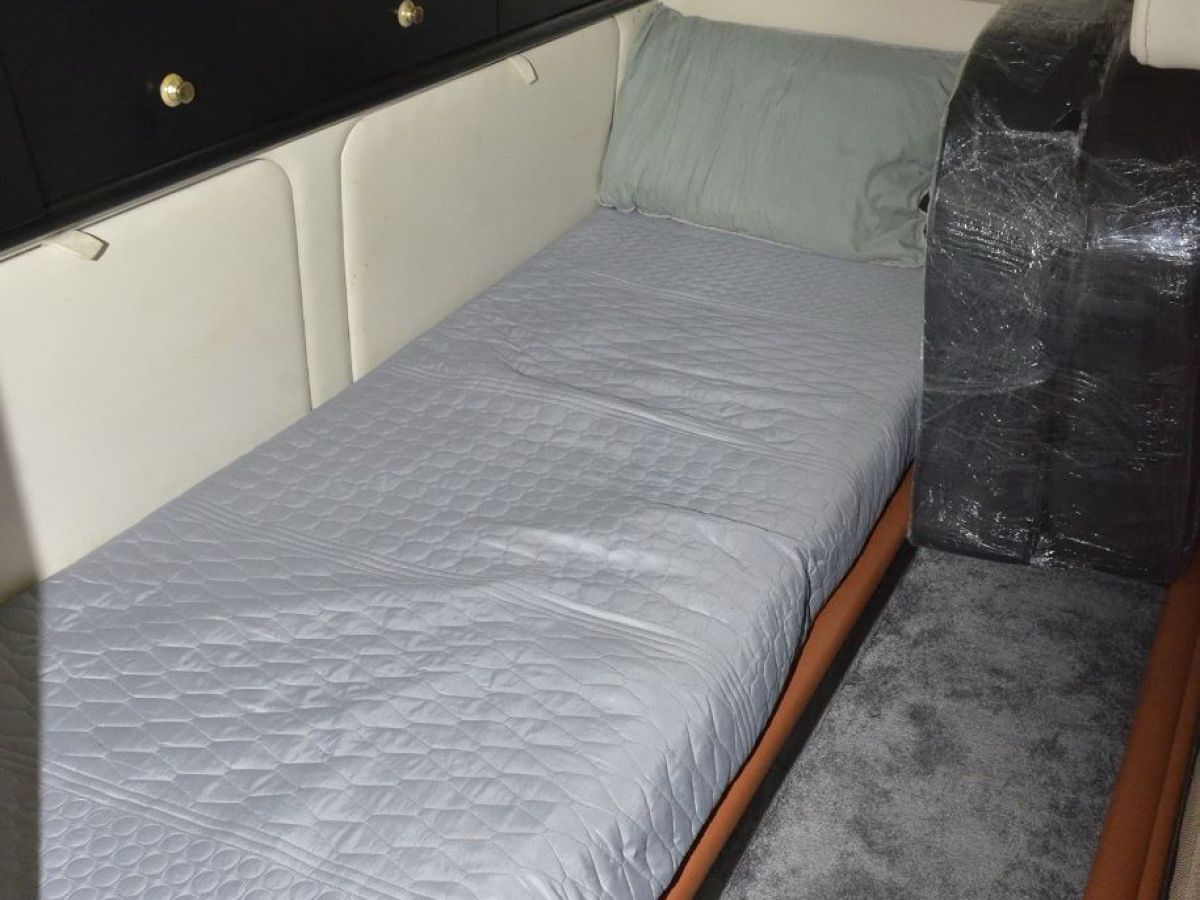 Narrow boat cabin with a bed, gray bedding, and black storage cabinets.