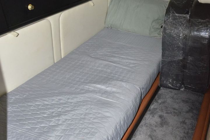 Narrow boat cabin with a bed, gray bedding, and black storage cabinets.