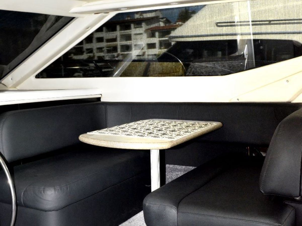 Boat interior with black seats, small table, and control panels.