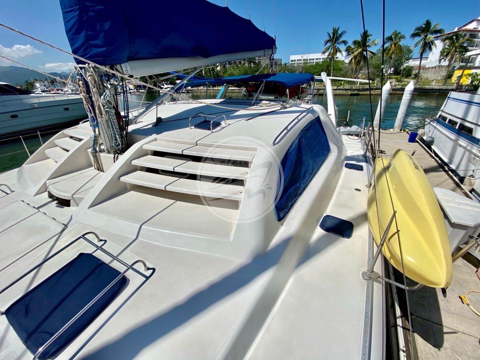 Sailboat deck with blue canopy, moored by palm trees and clear sky.