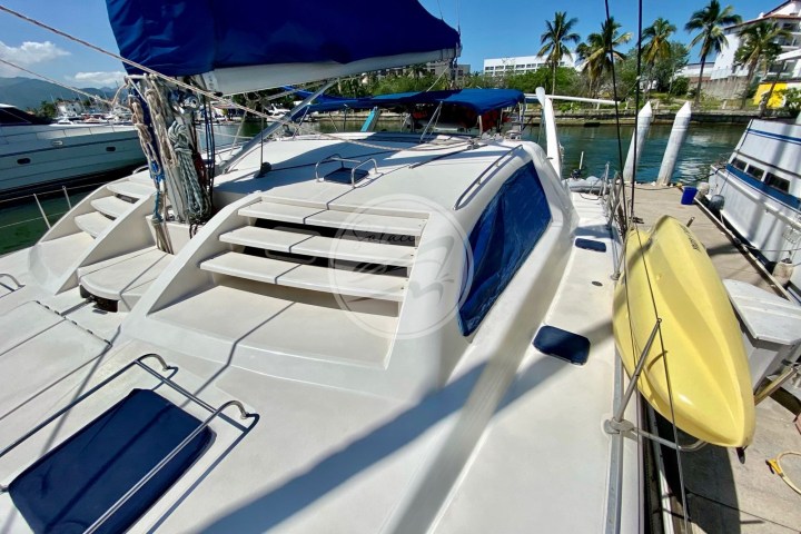 Sailboat deck with blue canopy, moored by palm trees and clear sky.