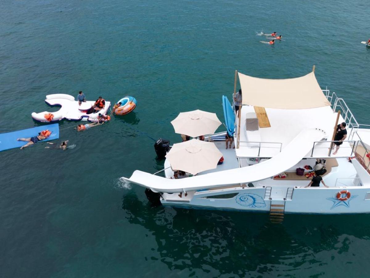 Boat with water slide and people swimming on floating mats in the ocean.