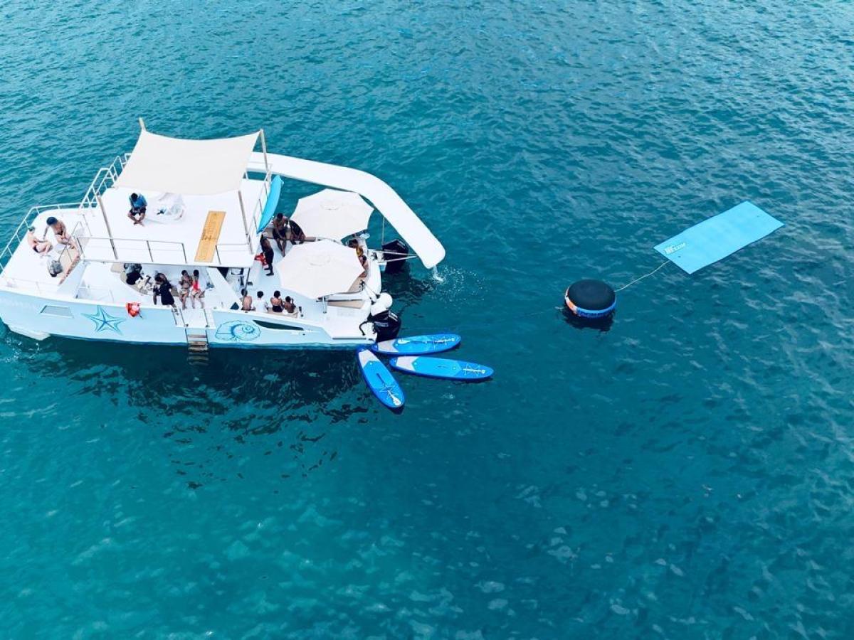 A boat on blue water with people onboard and floating mats nearby.