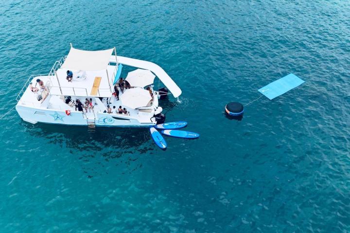 A boat on blue water with people onboard and floating mats nearby.