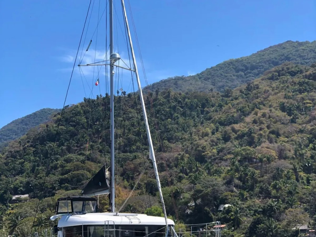 A white sailboat anchored in blue water with green hills and trees in the background.