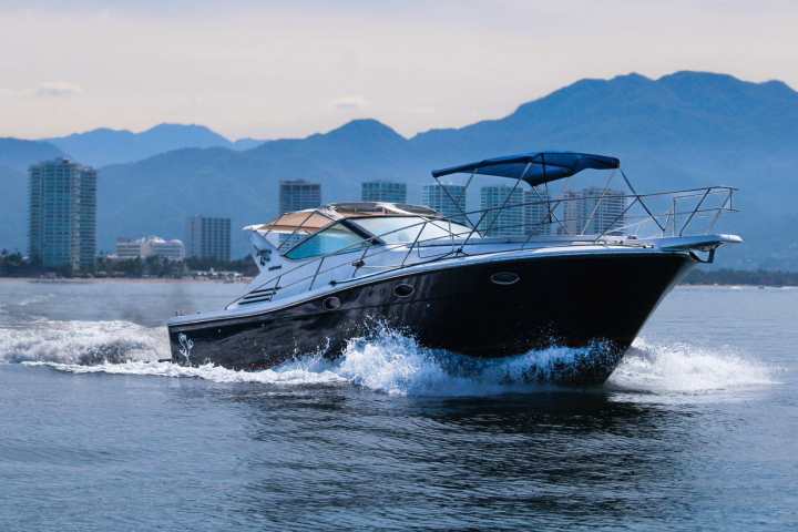 Motorboat cruising on water with city skyline and mountains in background.
