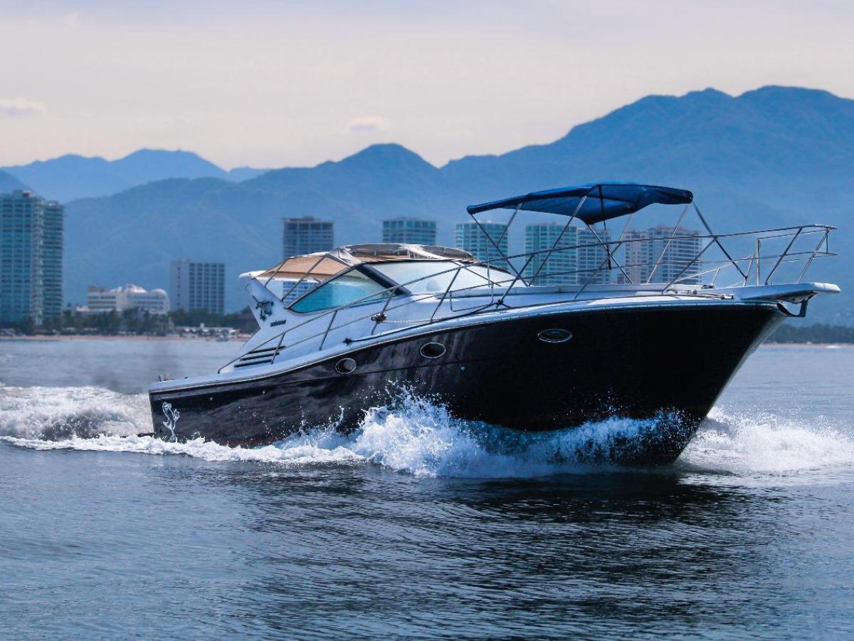 Motorboat cruising on calm water with city skyline and mountains in the background.