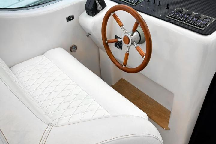 White boat cockpit with a wooden steering wheel and control panel.